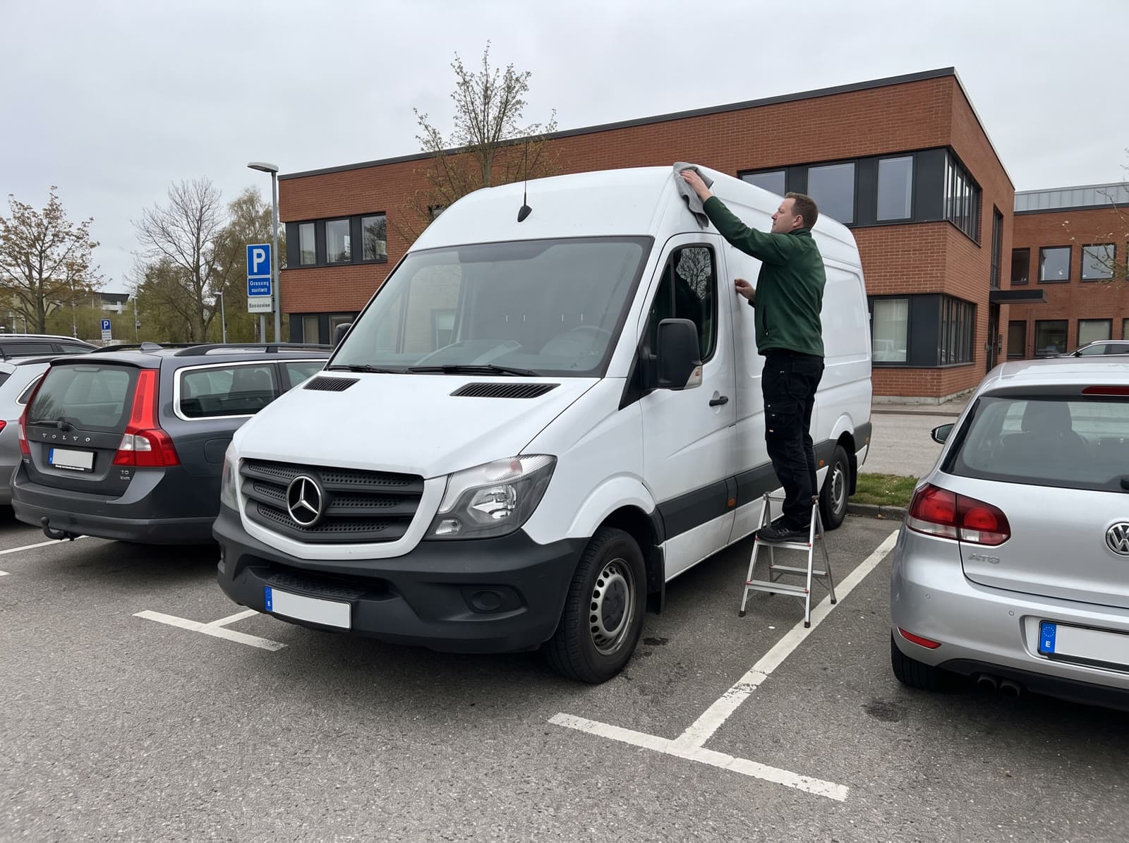 Tvättare på en fristående stege torkar taket på en Mercedes Sprinter i Malmö
